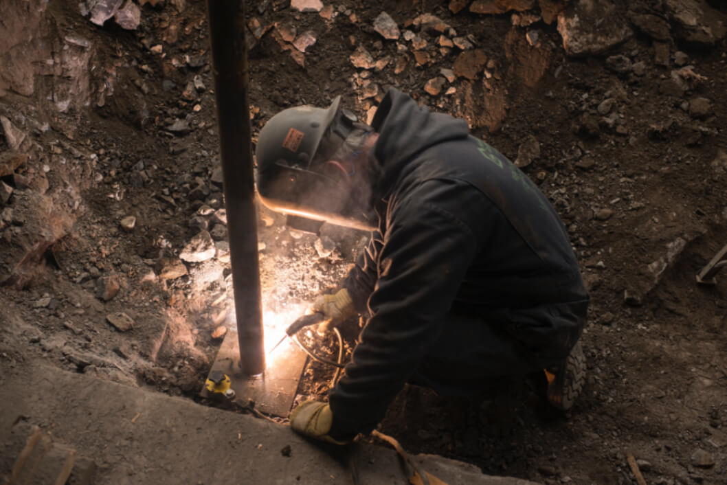 Un travailleur soudant des piliers d’acier à des plaques d’acier pour étayer une fondation